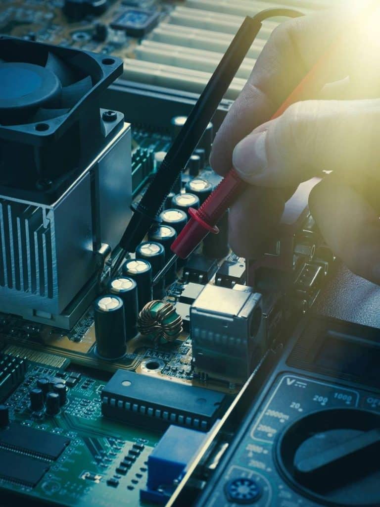 Technician inspecting a motherboard with a multimeter.