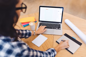Small business owner working at a laptop with a notebook, coffee, and colorful folders on a wooden desk.