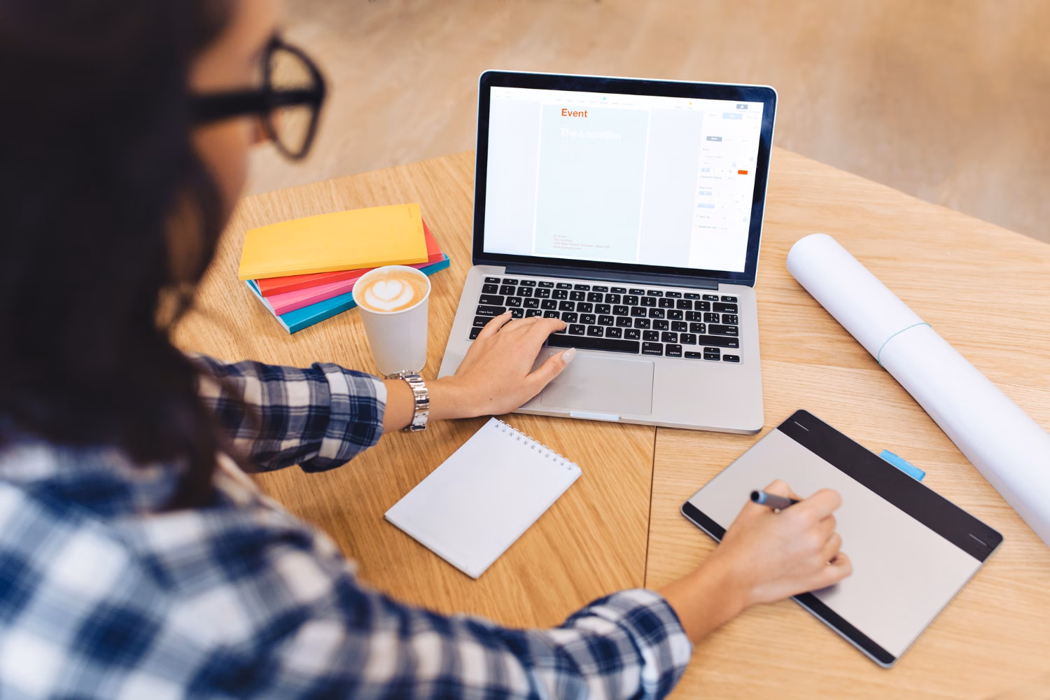 Small business owner working at a laptop with a notebook, coffee, and colorful folders on a wooden desk.