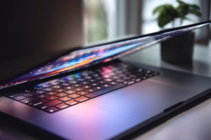 Close-up of a modern laptop with a partially closed screen, reflecting colorful light on the keyboard in a home office setting