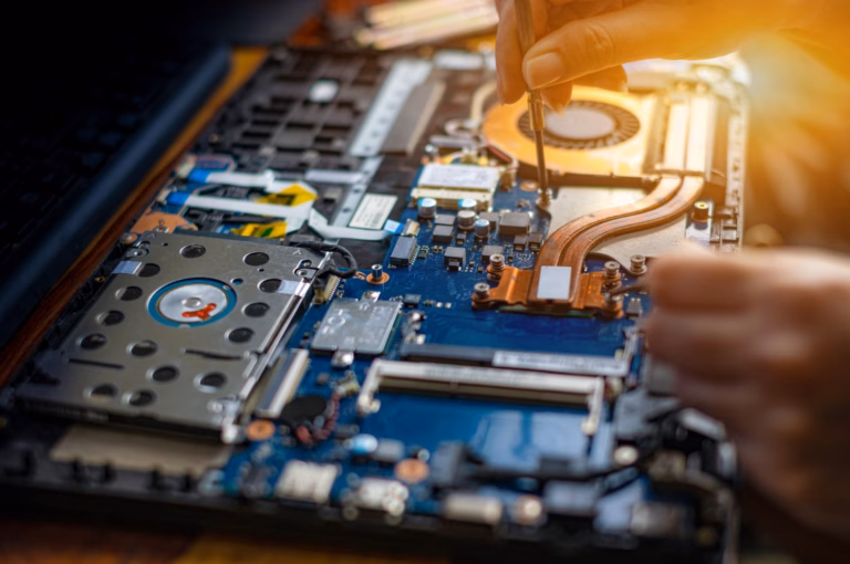 Hand using a screwdriver to inspect laptop internals, highlighting RAM and storage components