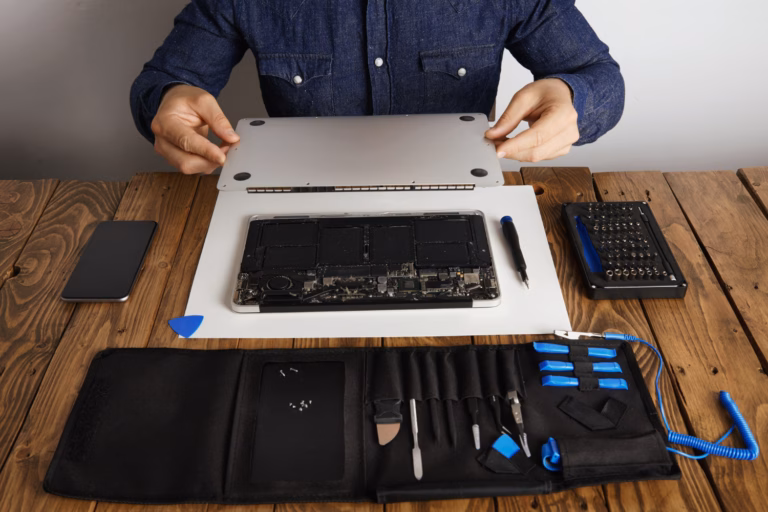 Person opening a laptop with repair tools on a wooden desk — illustrating a decision between repairing or replacing a laptop.