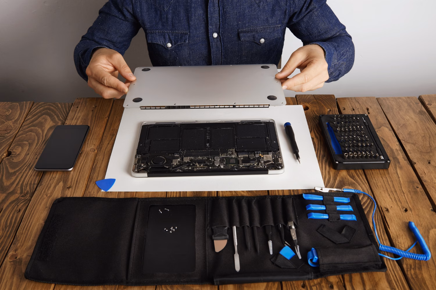 Person opening a laptop with repair tools on a wooden desk — illustrating a decision between repairing or replacing a laptop.