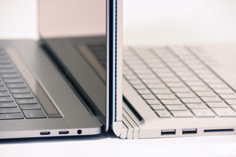 Close-up of MacBook and Windows laptop side by side, highlighting design differences for a comparison guide.